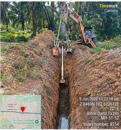 Red HDD rig pulling dark pipe through trench, worker in hi-vis and yellow boots standing beside rig with back to camera. Drill rods staged on lorry behind. MH 4–5, Index 205 (24 February 2026).